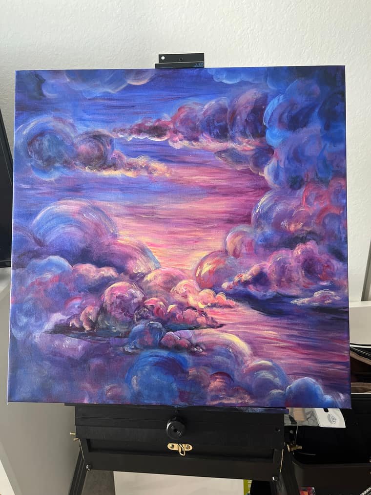 Painting of billowing violet and pink clouds over a glowing sunset sky, on an easel