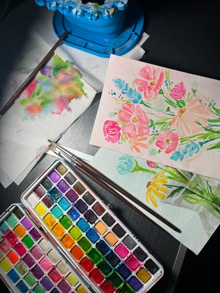 Two watercolor flower studies in pink and coral beside an open watercolor palette