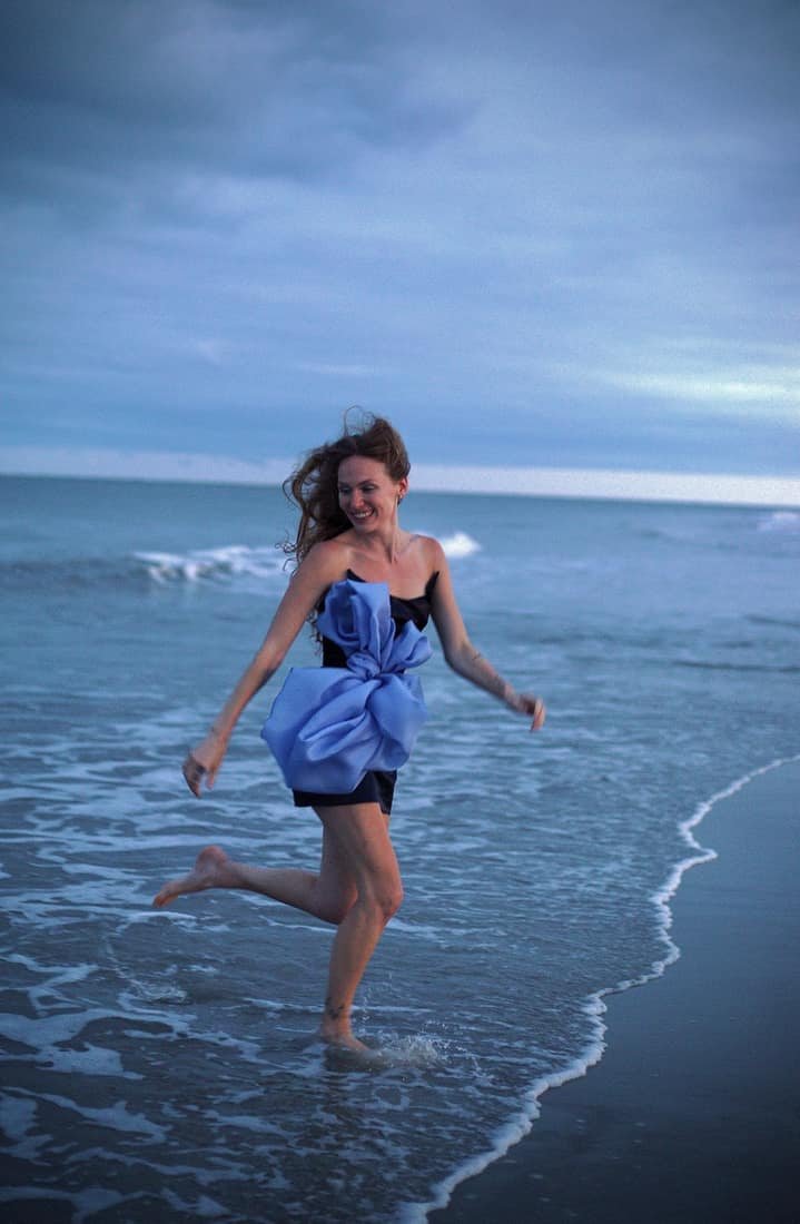 Model in a periwinkle bow dress running through the surf at dusk, from the Neverland collection
