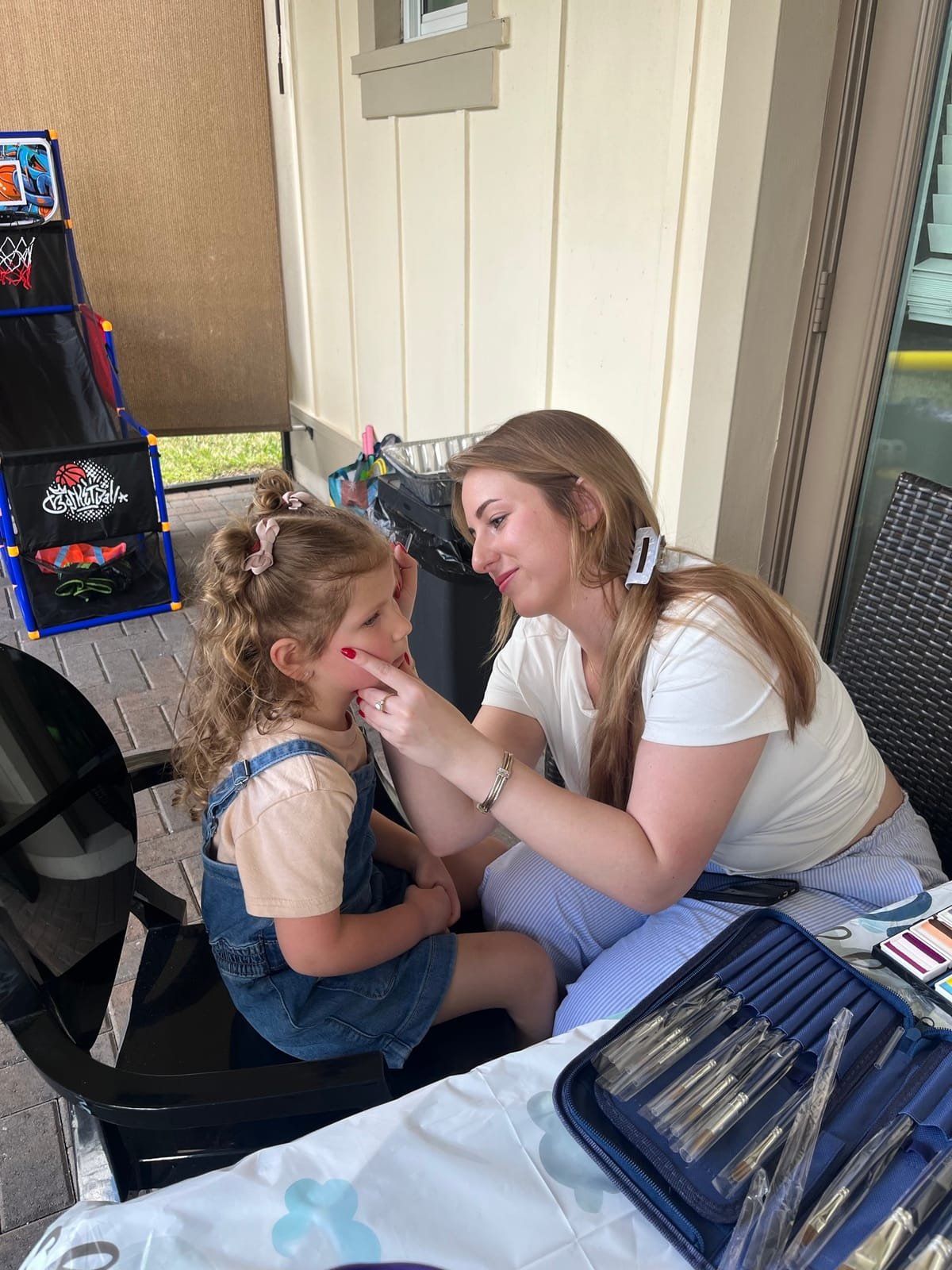 Jules face-painting a little girl's cheek at an outdoor event