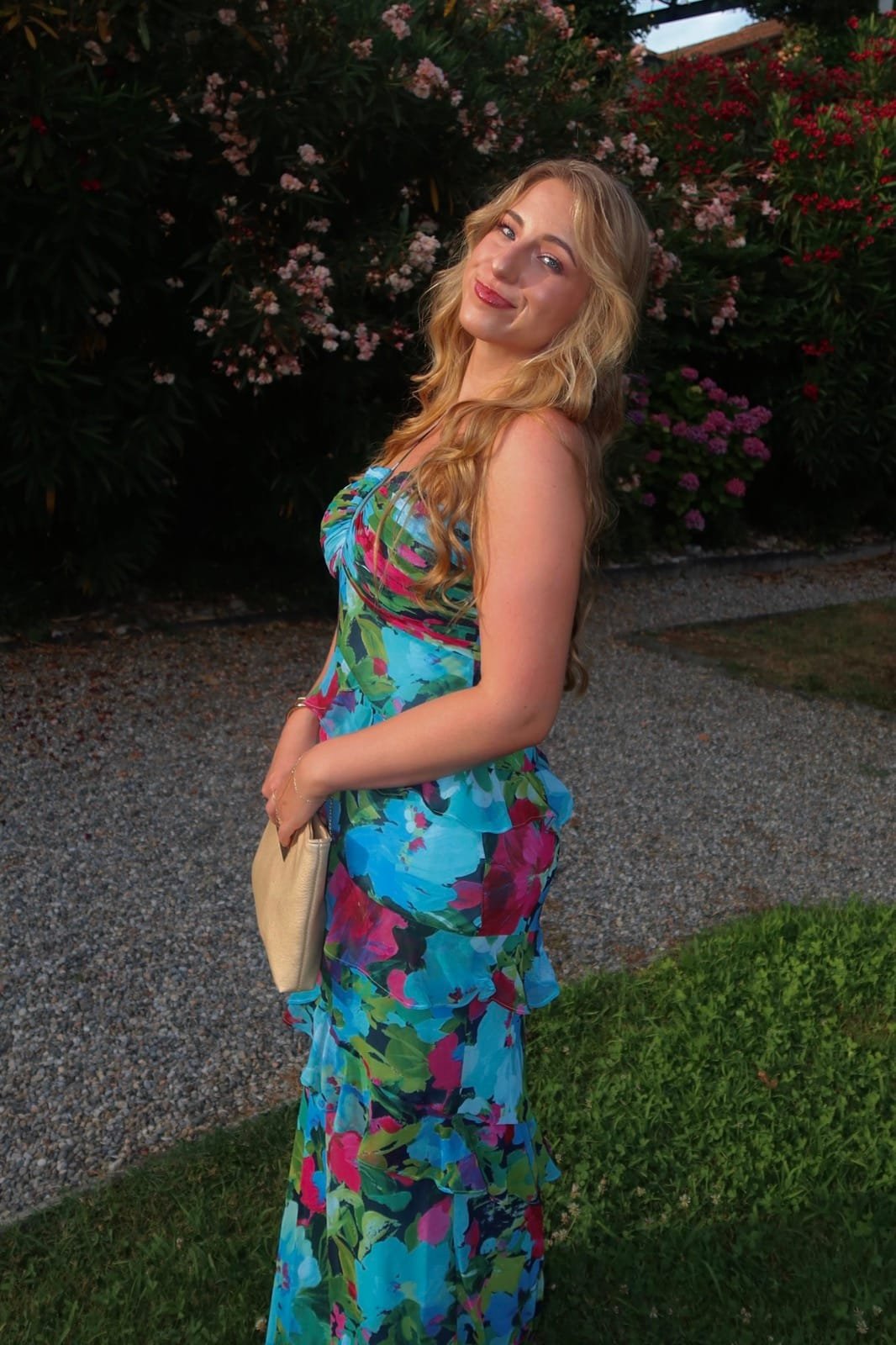 Jules Amber in a floral dress, smiling over her shoulder in a garden