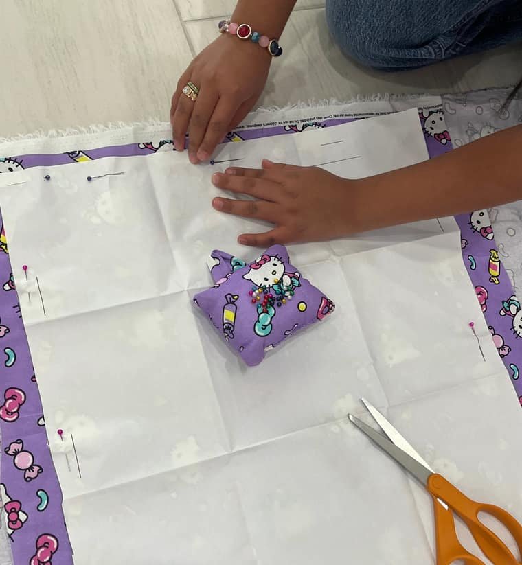 A young student pinning and cutting purple character-print fabric in sewing class